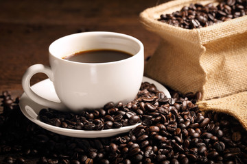 warm cup of coffee with sack inside by coffee bean on wood background