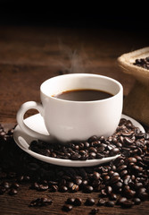 warm cup of coffee with sack inside by coffee bean on wood background