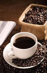 warm cup of coffee with sack inside by coffee bean on wood background