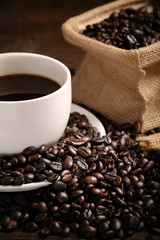 warm cup of coffee with sack inside by coffee bean on wood background