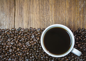 a cup of black coffee with coffee beans on wooden background