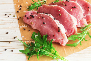 Fresh raw pork meat with salt, pepper and arugula.