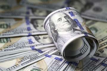 Roll of hundred dollar bill on dollar bills background.