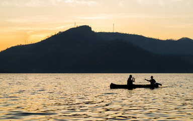 silhouette of two men are boating in the dam on the morning.