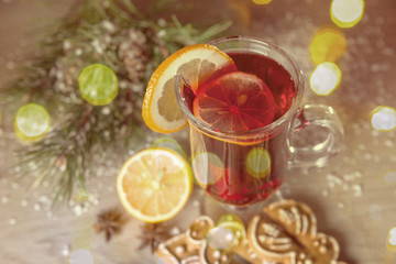 Mulled wine with lemon and cinamon sticks in glass and christmas cookies on the wooden table with christmas tree branch and snow