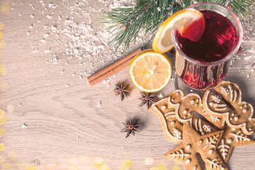 Mulled wine with lemon and cinamon sticks in glass and christmas cookies on the wooden table with christmas tree branch and snow