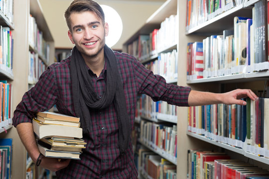 Smiling male student picking a book in a library