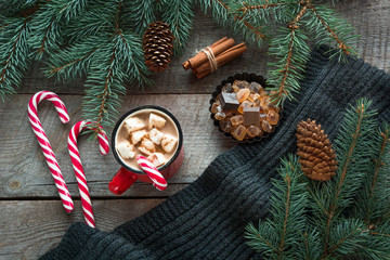 Mug hot coffee with milk, red candy cane on the wooden background with cone, branch of christmas tree and grey scarf. New Year. Holiday card. Rustic style. Top view and copy space.