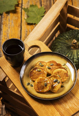 Pumpkin pancakes topped with honey and sprinkled with pumpkin seeds on a plate with the effect of craquelure on a wooden box with a cup of coffee and a bowl with honey. Selective focus 