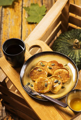 Pumpkin pancakes topped with honey and sprinkled with pumpkin seeds on a plate with the effect of craquelure on a wooden box with a cup of coffee and a bowl with honey. Selective focus 