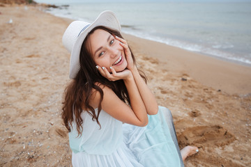 Cheerful lovely young woman sitting and smiling on the beach