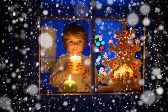 Little kid boy standing by window at Christmas time and holding