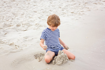 Little kid boy having fun with building sand castles