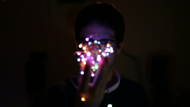 Young boy people with the glasses is playing with the Christmas Colored lights in his room.