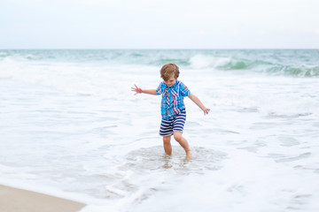 little kid boy running on the beach of ocean
