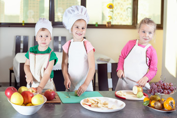 Three cute kids are preparing a fruit salad in kitchen