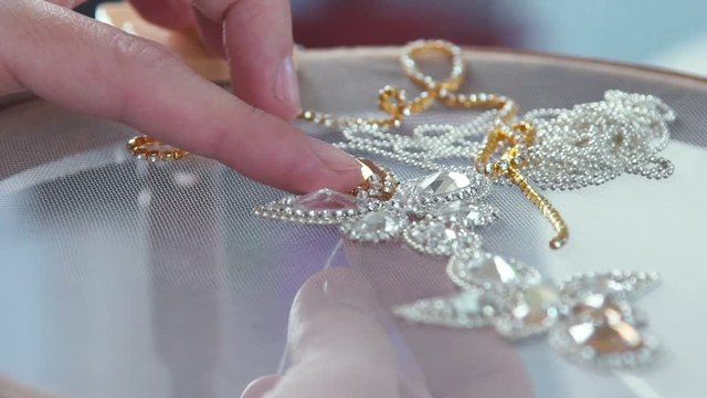 Master crafts embroider stones with the help of the hoop. The needle comes out of the canvas. Embroidery artificial shiny stones. Creating jewelry handmade jewelry. Decorative embroidery.