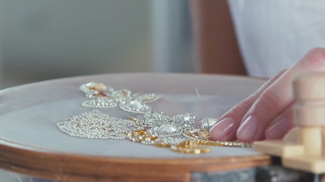 Slow motion. Close-up of mosaic stones diamond embroidery. Master crafts embroider stones with the help of the hoop. Creating jewelry handmade jewelry. Decorative embroidery. White-gold embroidery.