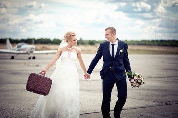 Young couple just married with a suitcase running on airplane