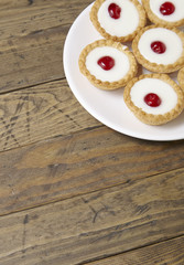 A plate full of freshly baked Bakewell tarts on a rustic wooden table top background with blank space below