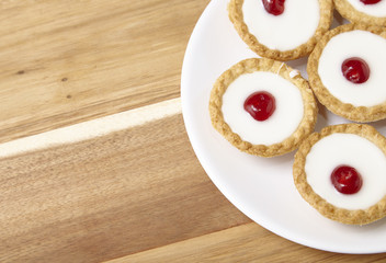 A plate full of freshly baked Bakewell tarts on a wooden kitchen counter top background with blank space at side