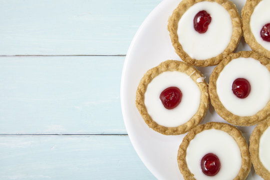 Aerial view of a plate full of freshly baked Bakewell tarts on a blue wooden table top background with blank space at side
