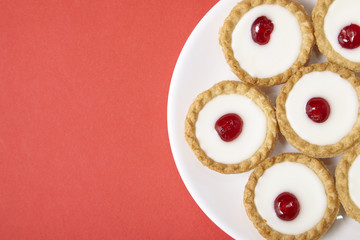 Aerial view of a plate full of freshly baked Bakewell tarts on a bright red background with blank space at side