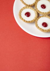 A plate full of freshly baked Bakewell tarts on a bright red background with blank space below