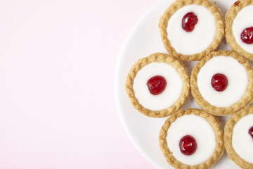 A plate full of freshly baked Bakewell tarts on a pastel pink background with empty space at side