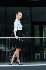 Young blonde businesswoman standing at the glass balcony