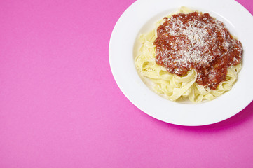 A dinner dish of spaghetti Bolognese on a bright pink background with blank space at side
