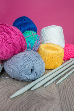 Knitting. Group of yarn and needles on grey wooden table  pink background. Handmade. Close up.