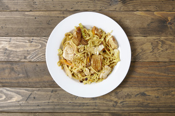 Aerial view of a dinner dish of chicken noodle stir fry on a rustic wooden table top background