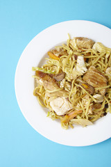 Overhead view of a dinner dish of chicken noodle stir fry on a bright blue background