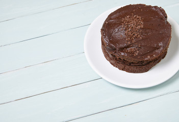 A whole chocolate fudge layer cake on a blue wooden table top background with blank space at side