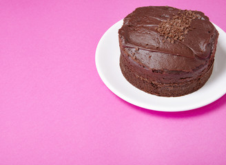 A whole chocolate fudge layer cake on a hot pink background with blank space at side