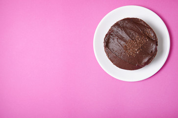 A whole chocolate fudge layer cake on a hot pink background with empty space at side