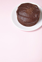 A whole chocolate fudge layer cake on a pastel pink background with blank space below