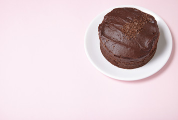 A whole chocolate fudge layer cake on a pastel pink background with empty space at side