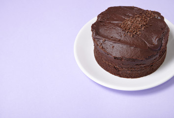 A whole chocolate fudge layer cake on a pastel purple background with empty space at side