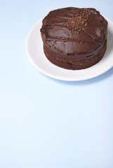 A whole chocolate fudge layer cake on a pastel blue background with empty space below