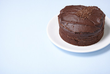 A whole chocolate fudge layer cake on a pastel blue background with empty space at side