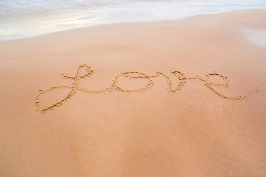 Love word drawn on wet sand by the waves on the shore. Background.