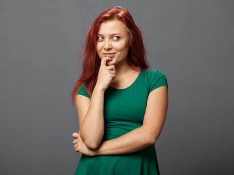 Young redhead woman in a thoughtful pose, gray background