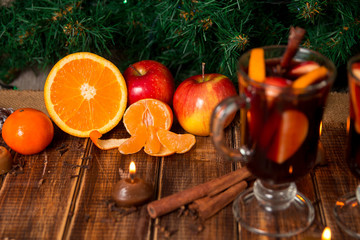 Christmas mulled wine with fruits and spices on wooden table. Xmas decorations in background. Winter warming drink  fruit ingredients around.