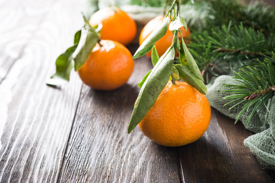 fresh tangerines with leaves and ripe mandarins with christmas tree on wooden table with copy space.