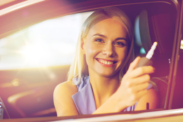 happy woman getting car key in auto show or salon