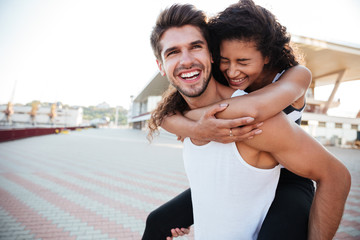Smiling young man carrying woman on his back outdoors