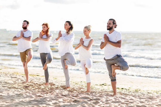people making yoga in tree pose on summer beach