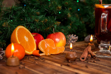 Fototapeta na wymiar Candles, fruits and spices on wooden table near mulled wine. Christmas decorations in background. New year.